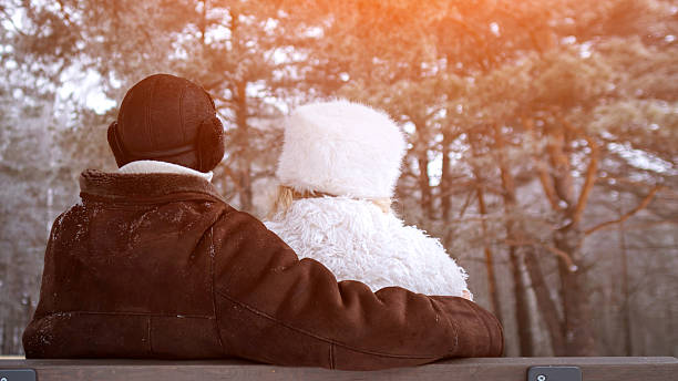 Senior Partners Seated In Peaceful Forest Scene, Older Couple Resting On Park Bench During Winter Twilight, Mature Pair Sitting Calmly On Park Bench Surrounded By Winter Woodland Landscape