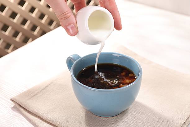 istock Woman pouring milk into cup with aromatic coffee at white table, closeup 2254706172