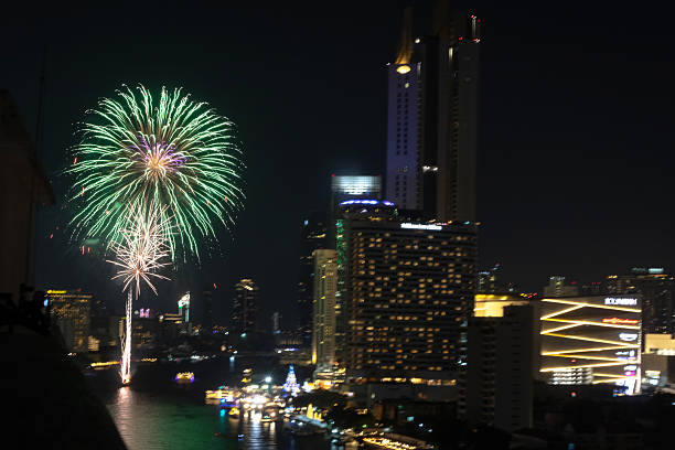 Bangkok, Thailand-December 9, 2024: Vibrant fireworks illuminate night skyline by the Choaphraya river with skyscraper in Bangkok, Thailand..