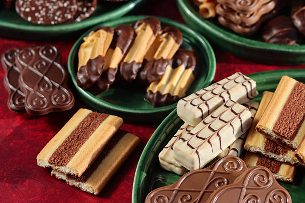Stock photo showing close-up, elevated view of an assortment of luxury collection of Belgian chocolate biscuits on green plates, pictured against a mottled red background.