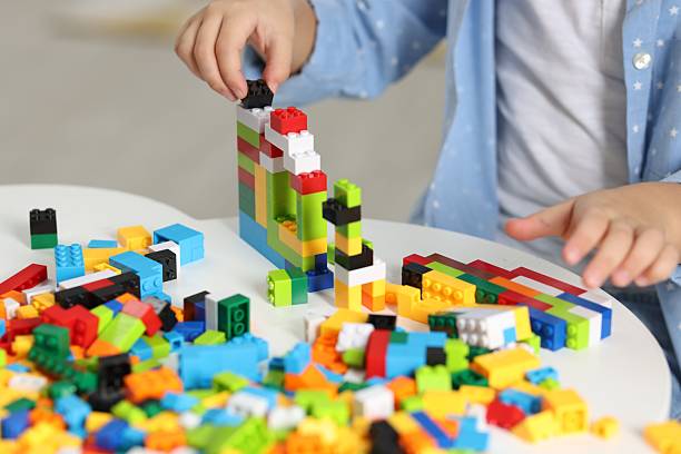 Girl playing with building blocks at white table indoors, closeup