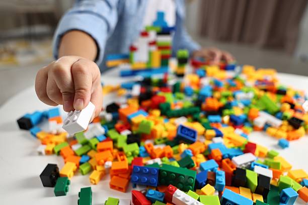 Girl playing with building blocks at white table indoors, closeup. Selective focus