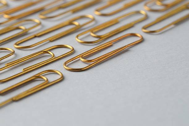 An abundance of silver paper clips on a wooden surface with one colored paperclip in amongst the uniform silver ones.