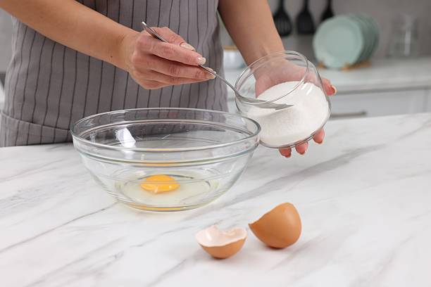 istock Making dough. Woman adding sugar into bowl with egg at white marble table, closeup 2254713254
