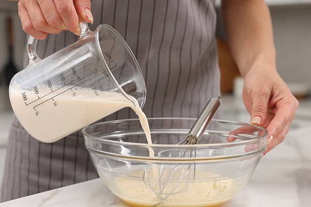 istock Making dough. Woman adding milk into bowl at white marble table, closeup 2254713303