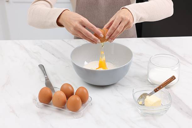 istock Making dough. Woman adding egg into bowl at white marble table, closeup 2254713405