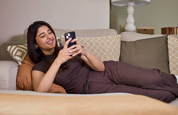istock Relaxed Woman at Home on Couch, Smiling While Using Smartphone in Cozy Living Room 2254716791