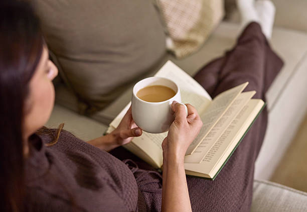 istock Cozy Home Moment: Person Reading a Book While Holding a Hot Drink on Sofa 2254716805