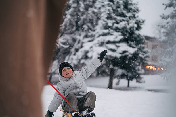 Young boy grinning on a sled as an adult pulls him through fresh snow, enjoying playful winter fun, family bonding and outdoor recreation on a frosty day