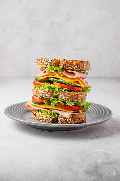 istock A triple sandwich with ham, cheese, lettuce, and vegetables on whole grain bread on a plate 2254720120