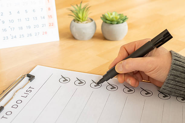 istock Person's hand marking completed tasks with a black marker on a to do list, showing organization, productivity, and goal achievement on a wooden desk with a calendar 2254720991