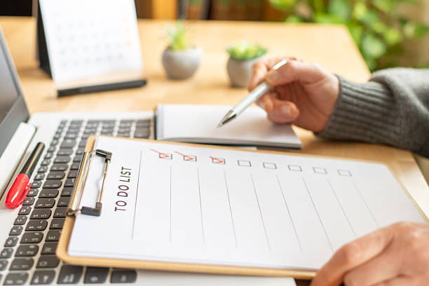istock Person's hand marking checked boxes on a clipboard to manage a to-do list while working at a laptop, organizing tasks and tracking progress for daily productivity and planning 2254721041