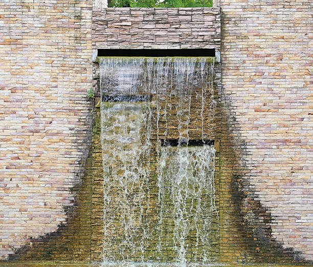 Artificial waterfall flowing down a modern decorative stone brick wall in a garden.