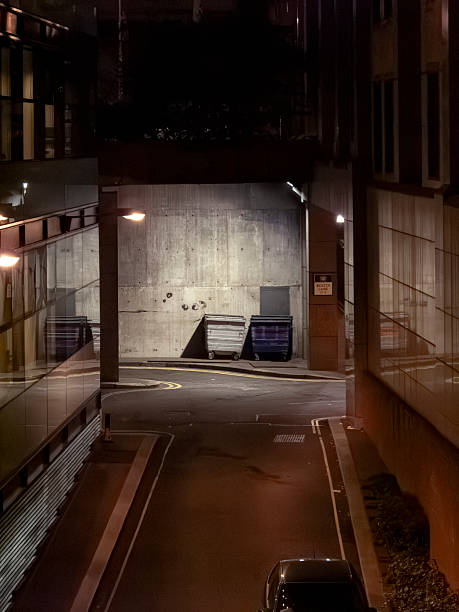 Modern concrete building exterior at night with waste bins and illuminated parking area showing urban infrastructure