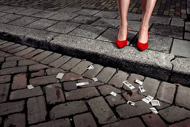 Artistic detail of legs in red heels standing on cobblestones with scattered vintage photographs showing creative urban photography concept