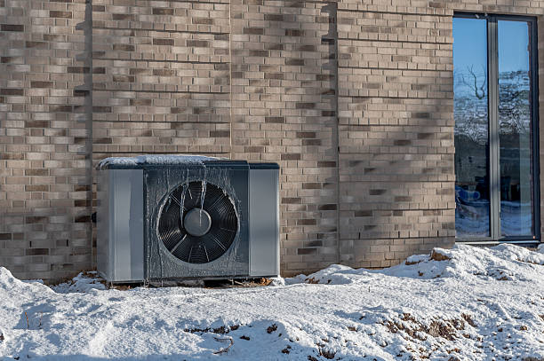 istock Air source heat pump unit with icicles hanging from casing installed against modern brick building surrounded by snow during winter. Energy-efficient residential heating technology. 2254724784