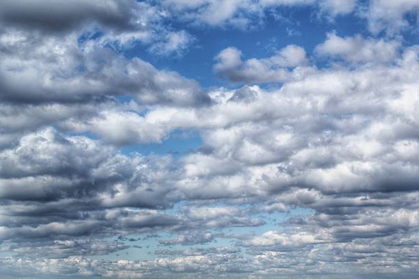 A dynamic sky filled with multiple layers of white and gray cumulus and stratocumulus clouds on a bright, partially blue day