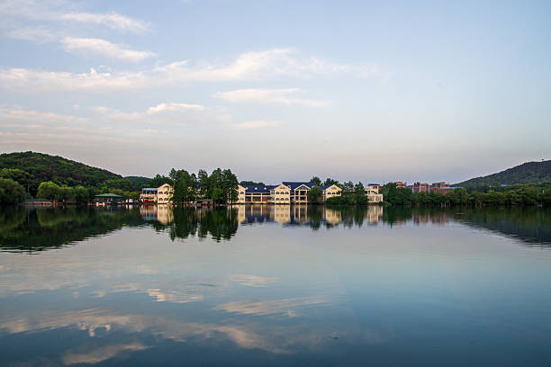 Scenic view of a large residential house or resort hotel located by a calm lake. The building is reflected in the water under a beautiful sunset sky with pink and blue hues. The concept conveys luxury living and vacation. Authentic real photography.