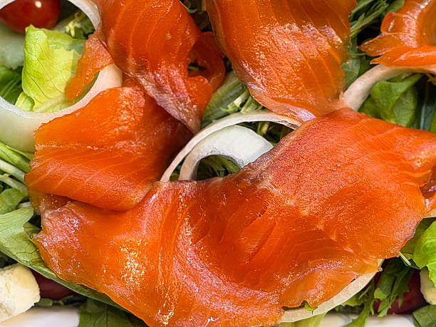 Stock photo shows fresh smoked salmon salad with crisp lettuce, cherry tomatoes, and sliced onions, emphasizing a healthy eating concept. Rich in omega-3 from oily fish, this vibrant dish highlights balanced nutrition and wholesome ingredients