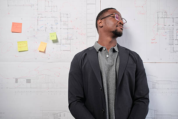 One smart young Black male architect in suit standing with design work on board, building construction blueprint with business concept ideas in studio company, happy and confident in presentation.