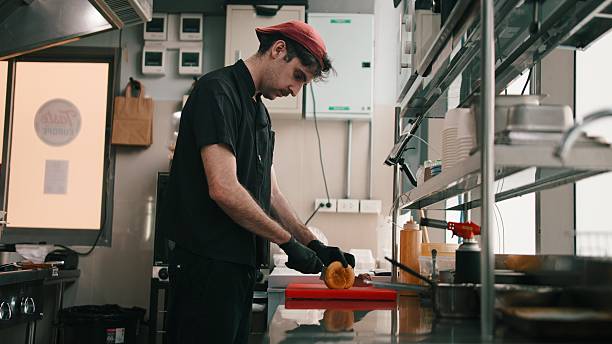 istock Chef working in a dark kitchen, slicing a burger bun on a red cutting board 2254731119