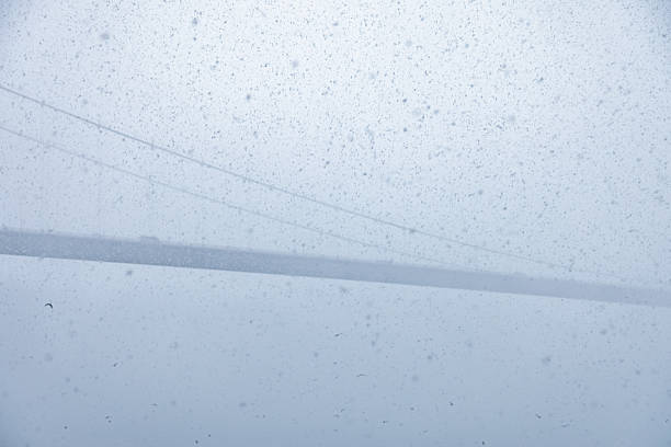 Istanbul, Turkey - Heavy snowfall and dense winter haze reduce visibility around the Bosphorus Bridge as the suspension structure fades into the white sky, creating a minimal and atmospheric scene where falling snow dominates the frame and the iconic bridge appears only as a faint silhouette across the Bosphorus Strait, emphasizing harsh winter weather conditions and limited visibility in Istanbul