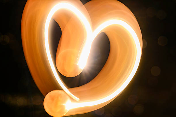 Abstract image featuring flowing light trails, creating curved lines with a warm, glowing tone. The light paints an organic, dynamic texture against a dark background