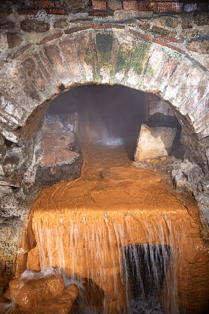 A flowing stream of thermal water in Bath, England, emerging from a stone archway, with a misty atmosphere and rocky surroundings