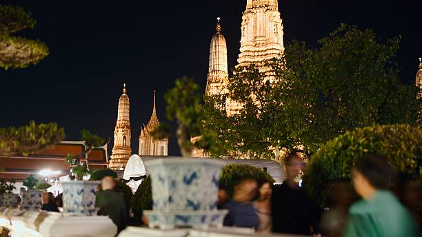 Wat arun's iconic temple spires glowing at night, creating an atmospheric scene with people
