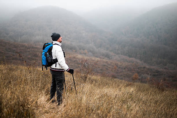 Hiker in warm clothing exploring winter hills with backpack and hiking poles. The atmospheric fog enhances the sense of freedom, vitality and connection with nature.