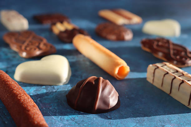 Stock photo showing close-up view of an assortment of luxury collection of Belgian chocolate biscuits, pictured against a mottled blue background.