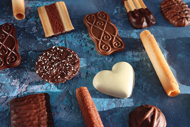 Stock photo showing close-up, elevated view of an assortment of luxury collection of Belgian chocolate biscuits, pictured against a mottled blue background.