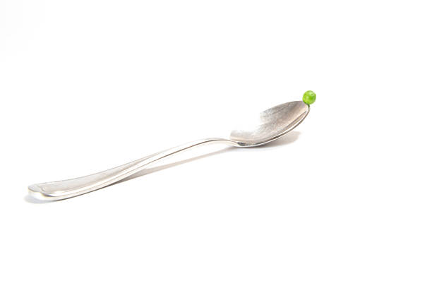 A green pea sitting on the tip of a table spoon