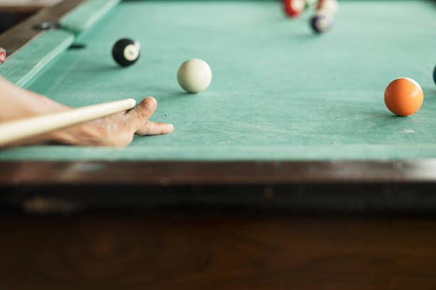 a hand with a cue takes aim at a cue ball among a group of balls on the billiard table, playing billiards in âeightâ, blurred background, blur