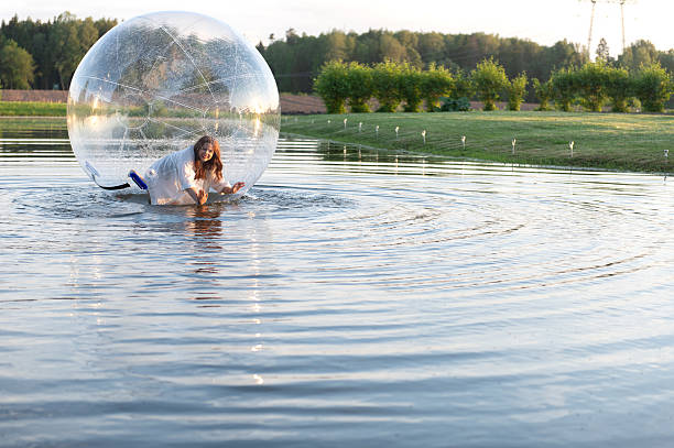 istock Water ball (similar to zorb or Human Hamster Ball) with young woman inside on pond surface 2254756600
