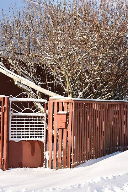Vertical photo of a red wooden fence with a mailbox. Winter rural scene with snow, calm atmosphere, copy space.