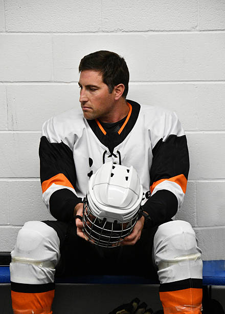 A handsome ice hockey player is sitting in the locker room looking contemplative before joining his team on the ice,