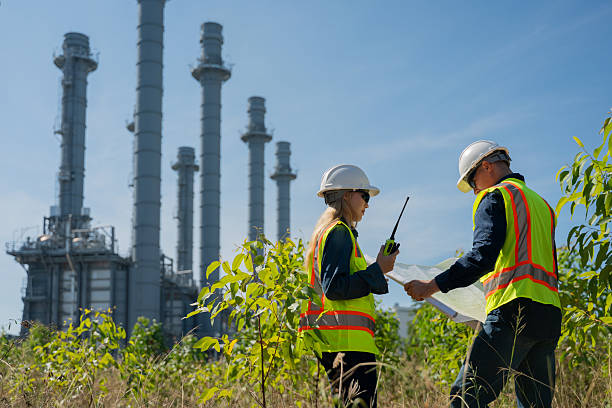 istock Industrial engineer wearing safety helmets and vests inspection technical plan and data on tablet with tall refinery towers rise background is industrial safety and carbon credit environment operations concept. 2254762717