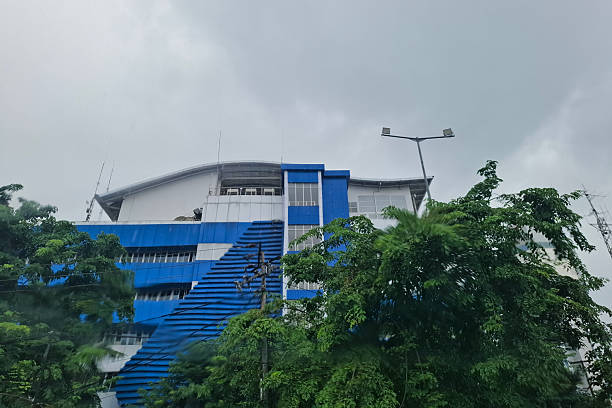 Modern Blue And White Office Building With Lush Green Trees Under A Cloudy Sky