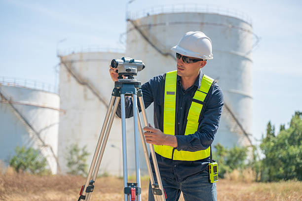 istock Engineer or worker site inspection or surveying activity industrial  tripod suggesting the work may involve geodetic or structural measurement tasks with oil refinery background. 2254764199
