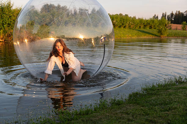 istock Water ball (similar to zorb or Human Hamster Ball) with young woman inside on pond surface 2254769188