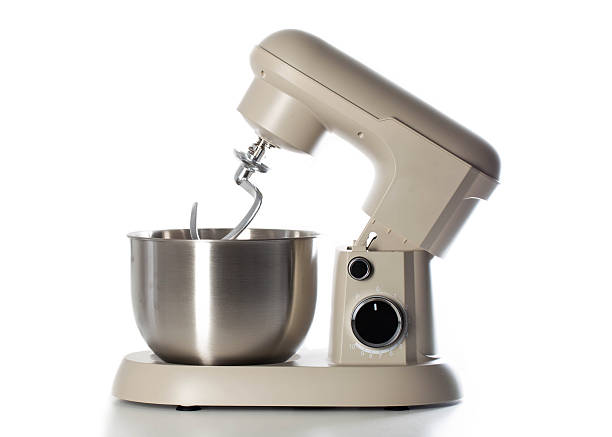 Close up view of contemporary cream colored electric stand mixer with shiny metal mixing bowl and dough hook attachment, showcasing design functionality for culinary tasks, home cooking