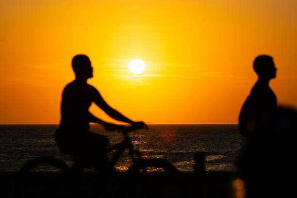 Elevated view of mature women walking and talking with bicycles on beach at sunset, Finale Ligure, Liguria.