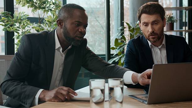 istock Two multiethnic company men workers business team busy with online project diversity employers multiracial businessmen discussing deals task in office. Caucasian African American partners with laptop 2254775877