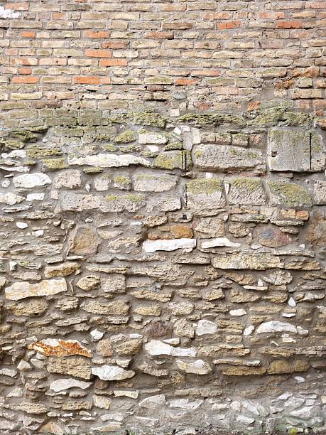 Old mixed gray stone and red brick masonry wall with green moss and rough mortar.