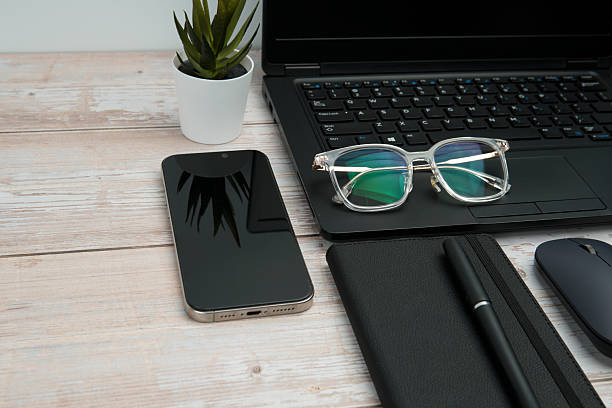 istock Top view business workspace with laptop, smartphone, eyeglasses, notebook, and mouse on white wooden desk representing productivity, digital work, and professional office setup with clean copy space. 2254777864