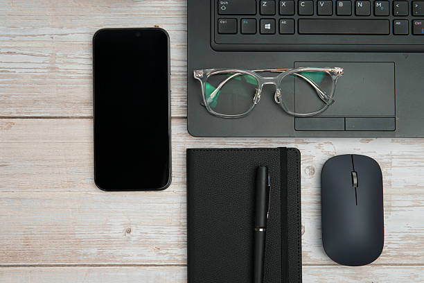 istock Top view business workspace with laptop, smartphone, eyeglasses, notebook, and mouse on white wooden desk representing productivity, digital work, and professional office setup with clean copy space. 2254777866