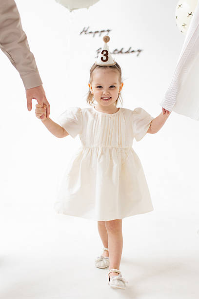 A happy little girl celebrates her third birthday, holding hands with her parents.