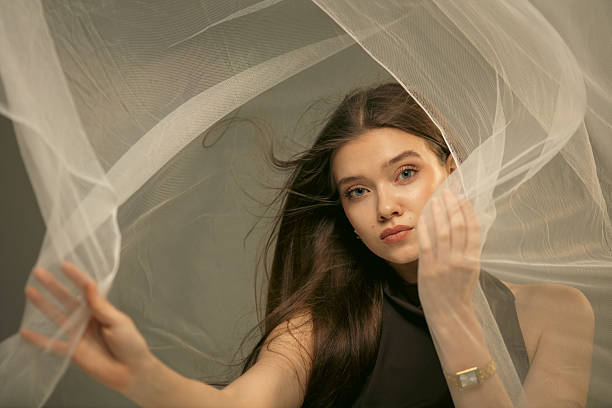 Portrait of beautiful female teenager model with long brown hair surrounded by curtains