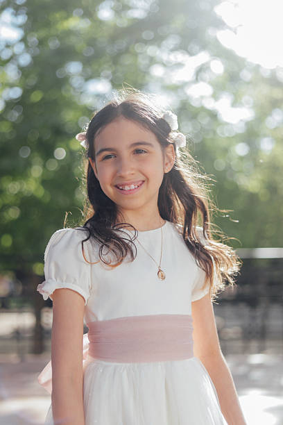 Portrait of a 10-year-old girl radiantly smiling with her hands on her chest, wearing a white shirt against a white background.